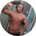 Shirtless man flexing his arm and looking at the camera in a round-framed selfie.