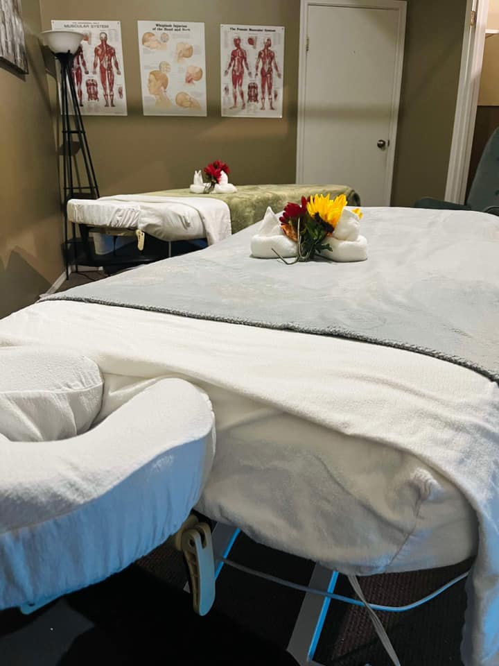 Two massage tables in a therapy room with flowers and anatomy posters on the wall.