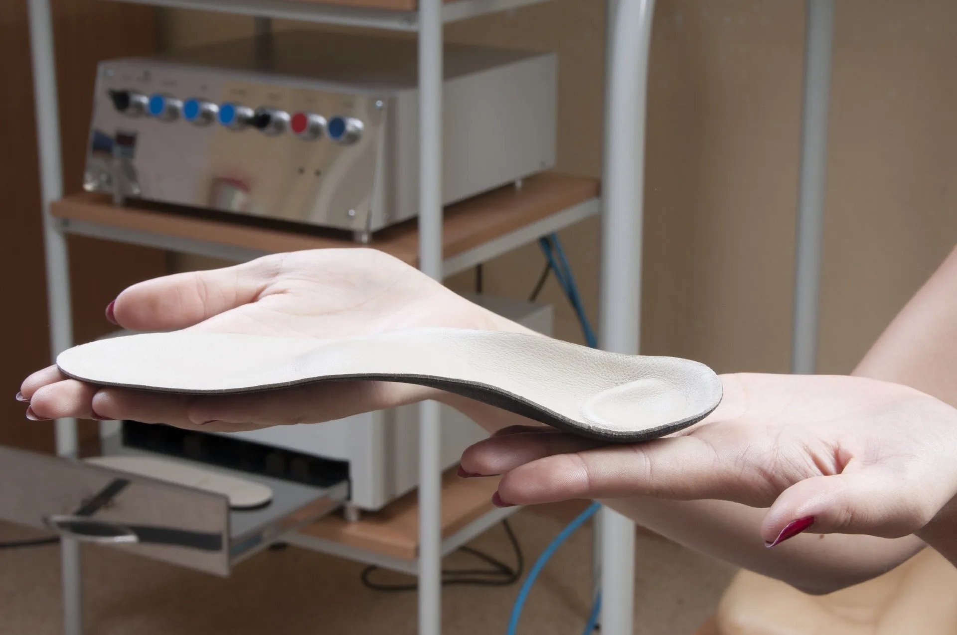 Hands holding a beige orthopedic shoe insole with arch and heel support.