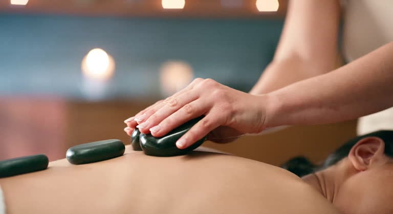 Close-up of a hot stone massage on a person's back with candles softly lit in the background.