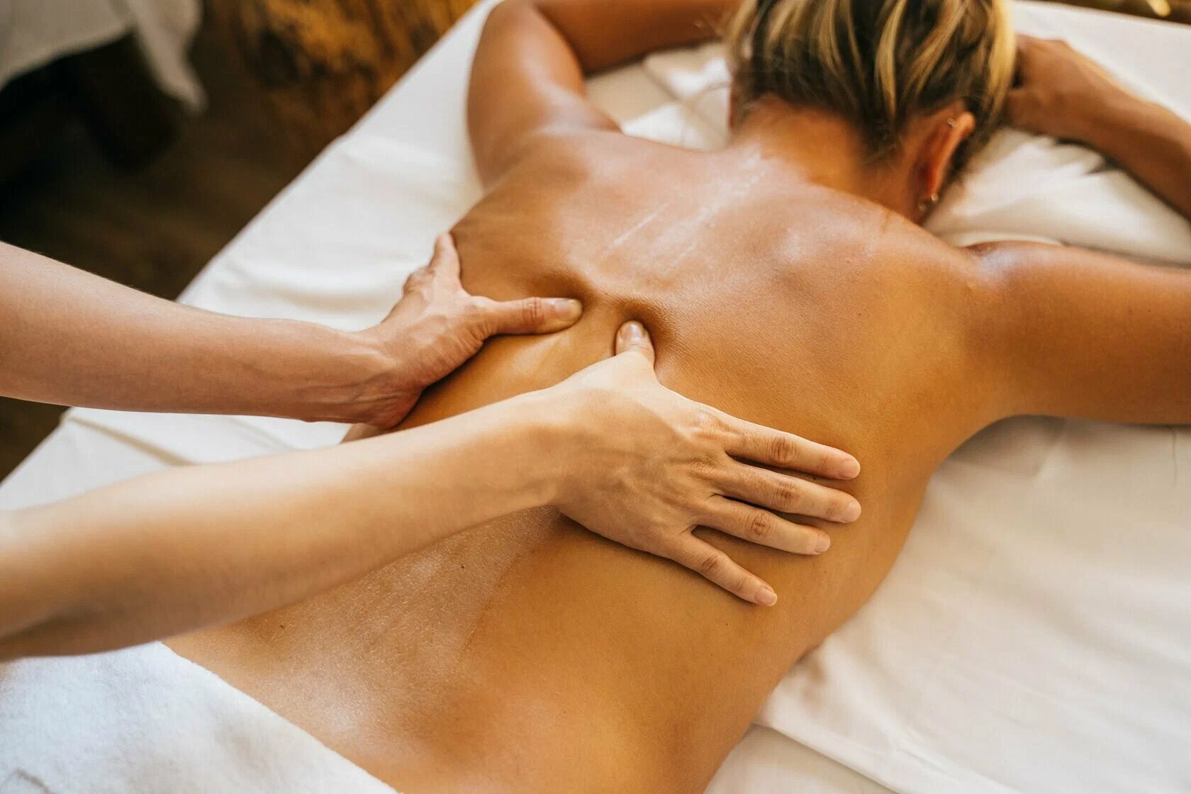 Person receiving a back massage lying face down on a white massage table.