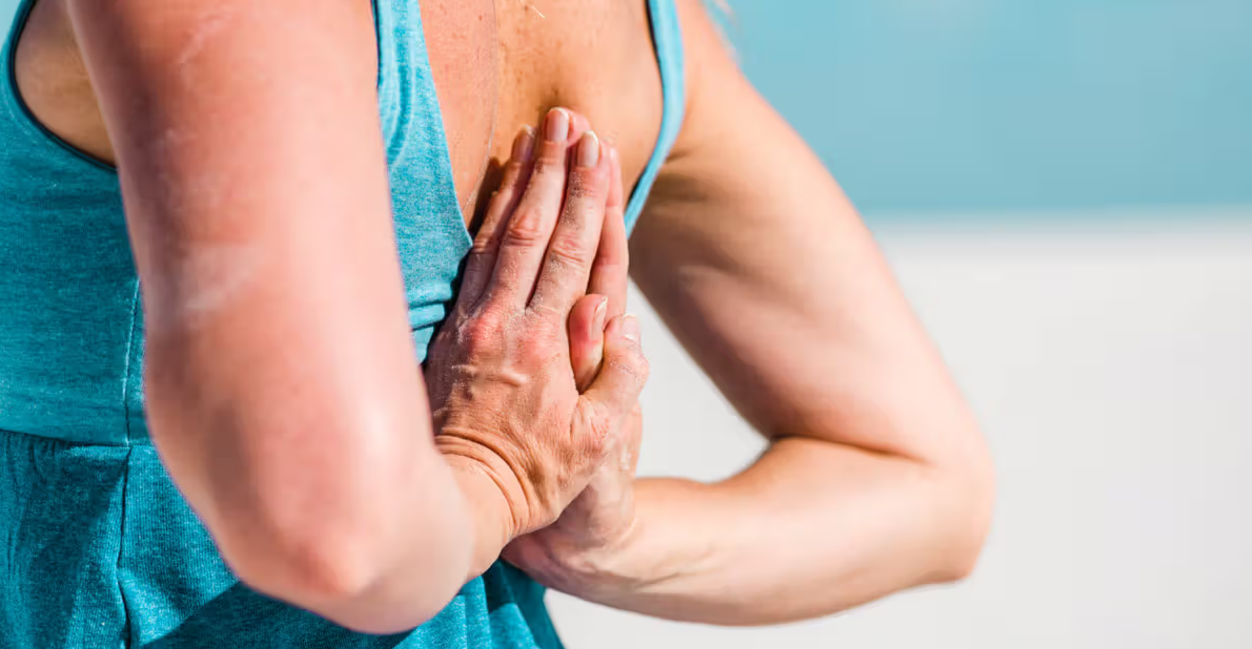 Person in teal tank top doing yoga pose with hands pressed together behind back.