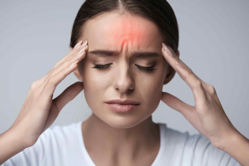 Woman with eyes closed, holding her temples, showing forehead redness indicating headache pain.